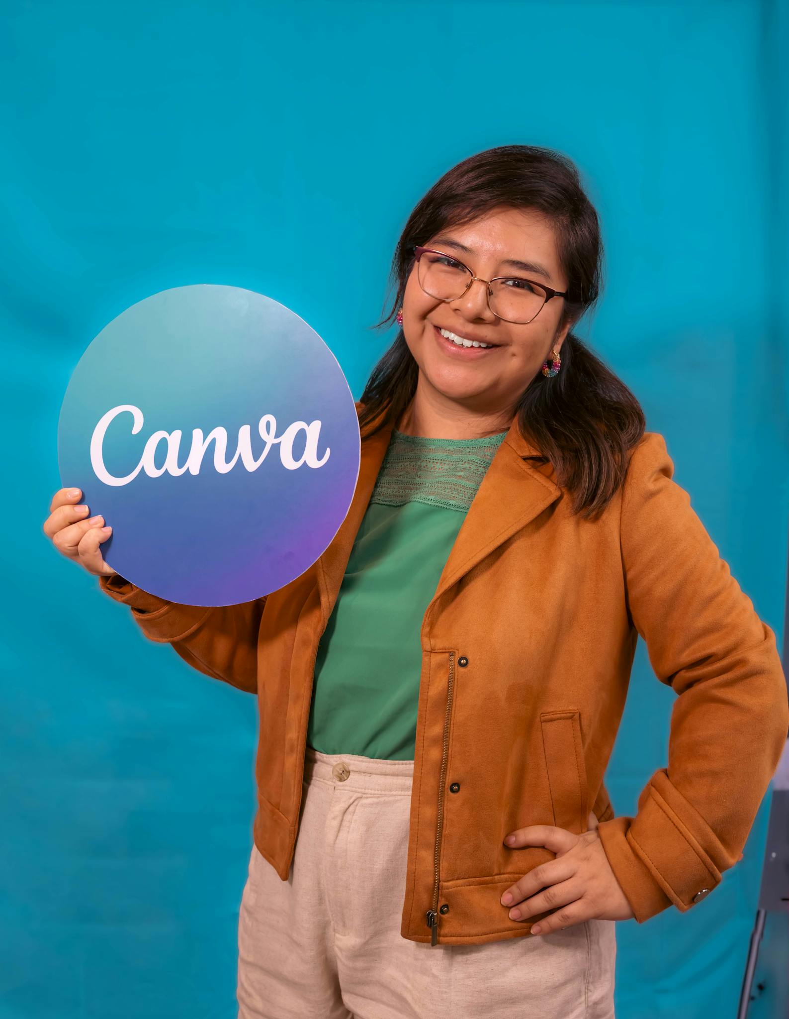 A smiling woman in a casual outfit holds a Canva sign, posing confidently against a vibrant blue backdrop.